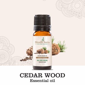 May include: A bottle of cedarwood essential oil with a black cap and a label that reads "Shudh Aura." The label also states "100% Pure & Natural." The image includes pine cones and the text "CEDAR WOOD Essential oil."