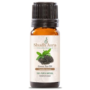 May include: A brown glass bottle of Green Tea Oil by Shudh Aura. The label features text and an illustration of green tea leaves. The bottle has a black cap and is labeled as 100% pure and natural, therapeutic grade.