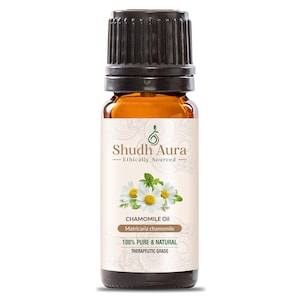 Op de afbeelding: Een bruine glazen fles kamille-olie met een zwarte dop. Het etiket bevat de tekst "Shudh Aura - Ethically Sourced" en "Chamomile Oil". Het etiket bevat ook een illustratie van kamillebloemen. De tekst "100% Pure & Natural" is ook zichtbaar.