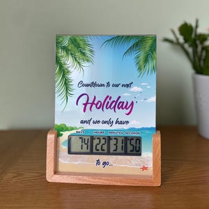 May include: A digital countdown clock in a wooden frame, featuring a beach scene. The clock shows "Countdown to our next Holiday" and the remaining time: 74 days, 22 hours, 31 minutes, and 50 seconds. The text "to go..." is also visible.