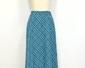 May include: A long teal skirt with a white and teal geometric pattern. The skirt has a fitted waist and a flowing, A-line silhouette.