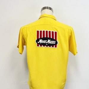 May include: Yellow short-sleeved shirt with a red and white striped patch that says "Moor Mans" in black lettering.