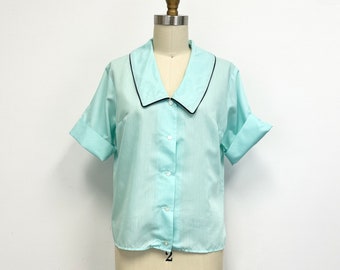 May include: A light blue short-sleeved button-up shirt with a wide, black-trimmed collar.