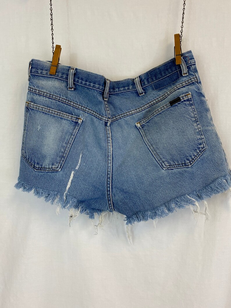 Pu&ograve; includere: Un paio di pantaloncini di jeans blu chiaro con orlo sfrangiato. I pantaloncini hanno una tasca posteriore con un piccolo logo.