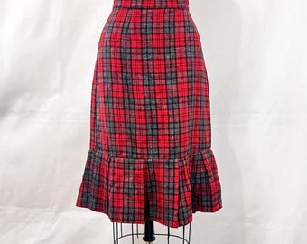 Könnte beinhalten: Ein rot-schwarz-grauer karierter Rock mit Rüschensaum. Der Rock wird auf einer Schaufensterpuppe präsentiert. Das Karomuster ist ein klassisches Design, und der Rock scheint aus einem gewebten Stoff zu sein.