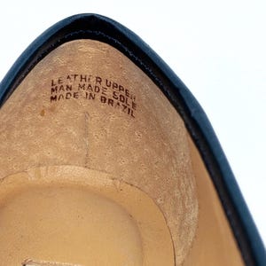 May include: Close-up of the interior of a navy blue shoe. The shoe's insole is tan, with the text "LEATHER UPPER MAN MADE SOLE MADE IN BRAZIL" printed on it. The shoe has a black trim.