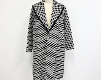 May include: A long, black and white houndstooth coat with a notched collar and black trim. The coat is displayed on a mannequin and has long sleeves. The coat is knee-length and has a classic, timeless design.