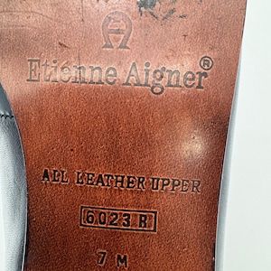 May include: Close-up of the sole of a shoe with the brand name "Etienne Aigner" embossed in the leather. The text "ALL LEATHER UPPER" is visible, along with the size "7 M" and style number "6023 R". The sole is brown.