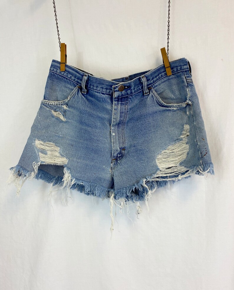 Pu&ograve; includere: Shorts di jeans consumati con bordi sfrangiati e pi&ugrave; strappi. I pantaloncini sono di colore blu chiaro e hanno un vita alta.
