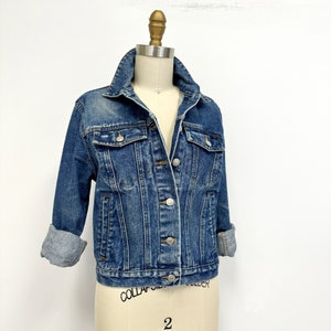 May include: A classic blue denim jacket with a button closure and two front pockets. The jacket has a slightly cropped fit and is made of a soft, comfortable fabric.