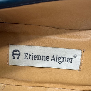 May include: Close-up of the interior of a shoe, featuring a tan leather insole. A rectangular label with the text "Etienne Aigner" is visible. The label has the brand's logo, a stylized "A" with a horseshoe shape.