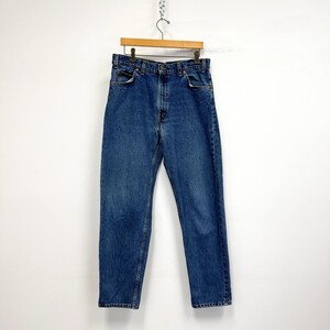 May include: Blue denim jeans hanging on a wooden hanger. The jeans have a classic five-pocket design, a button and zipper closure, and a straight leg fit. The denim has a medium wash with subtle fading.