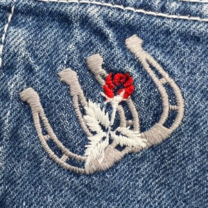 May include: Close-up of a pair of gray embroidered horseshoes with a red rose in the center on a blue denim background.