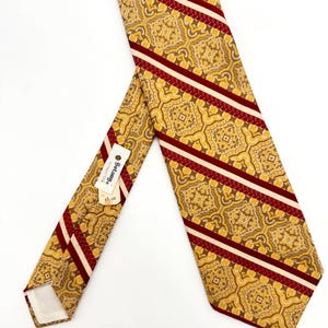 May include: A necktie featuring a repeating gold and brown geometric pattern accented by diagonal stripes in deep red and white. A white tag attached to the back displays the text Botany Wrinkle-Proof Ties and the price of $5.00.