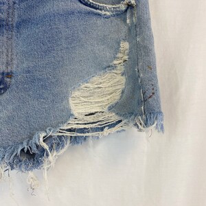 Pu&ograve; includere: Shorts di jeans blu chiaro con bordi sfrangiati e un aspetto consumato. I pantaloncini hanno una tasca anteriore e alcuni piccoli buchi.