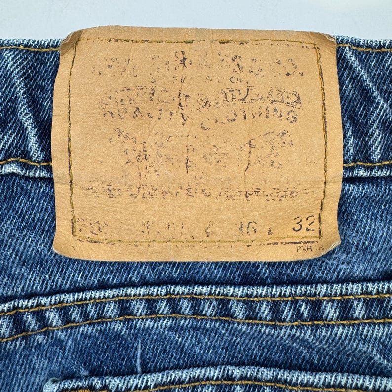 May include: Close-up of blue denim jeans with a brown leather patch. The patch has faded text and the numbers 36 and 32. The jeans have yellow stitching.