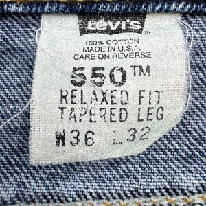 May include: Close-up of a Levi's jeans tag. The tag reads "550 TM RELAXED FIT TAPERED LEG W36 L32" and "100% Cotton Made in U.S.A.". The tag is white with black text, set against a blue denim background.