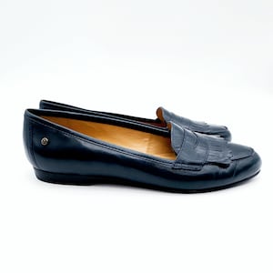 May include: A pair of navy blue leather loafers with a classic design. The shoes feature a rounded toe, a fringed vamp, and a small heel. The loafers are set against a white background.