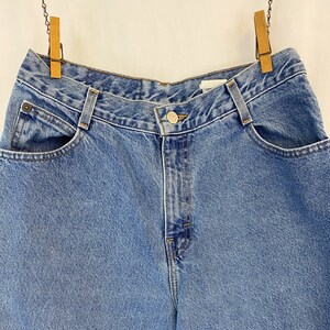 May include: Light blue denim jeans with a button closure and front pockets. The jeans are hanging from wooden clothespins. The denim has a classic, faded look.