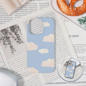 May include: A light blue phone case with a cloud design. The case features a sky blue background with white and light peach-colored clouds. The phone case is a protective accessory for a smartphone.