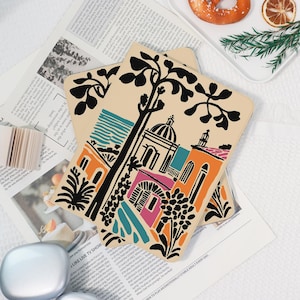 May include: Two beige decorative trays with a colorful architectural design featuring buildings, trees, and a dome. The design includes orange, teal, pink, and black elements. The trays are on a newspaper.