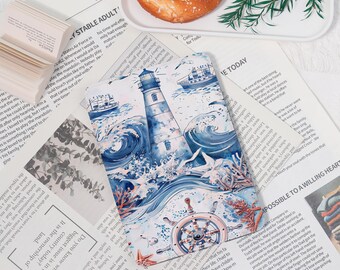 May include: A nautical-themed notebook featuring a lighthouse, ships, and waves in shades of blue. The notebook is open, revealing pages of text, and is placed on a newspaper with a pretzel on a white plate.