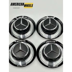 May include: Four black and silver car hubcaps with the AMG logo in white lettering. The hubcaps have a three-pointed star in the center.