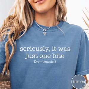 May include: Blue jean coloured t-shirt with the text "seriously, it was just one bite" in white. The text "Eve - genesis 3" is below the main text. A round blue jean coloured tag is in the bottom right corner.