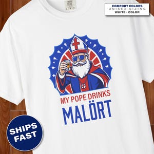 May include: White t-shirt with a cartoon illustration of a pope wearing sunglasses and holding a beer. The text "MY POPE DRINKS MALÖRT" is printed in blue. The shirt also has the text "COMFORT COLORS" and "UNISEX SIZING WHITE - COLOR".