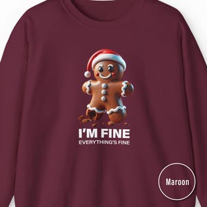 Op de afbeelding: Bordeaux sweatshirt met een peperkoekmannetje met een kerstmuts. Het peperkoekmannetje heeft een gebroken been en de tekst "I'M FINE EVERYTHING'S FINE" staat eronder gedrukt.