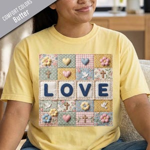 May include: A butter yellow short-sleeve t-shirt featuring a square patchwork graphic. The design includes the word LOVE in blue letters surrounded by squares with floral patterns, small 3D-style hearts, crosses, and white doves.