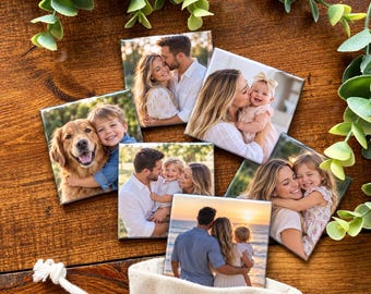 Pode incluir: Um conjunto de seis azulejos quadrados de cerâmica com várias fotografias de família impressas, incluindo imagens de casais, crianças e um golden retriever, dispostos sobre uma superfície de madeira com folhagem verde.
