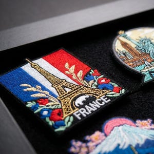 May include: A collection of embroidered travel patches featuring iconic landmarks including the Eiffel Tower with the text France, the Statue of Liberty with New York, a London scene, a Yosemite landscape, and Mount Fuji with cherry blossoms.