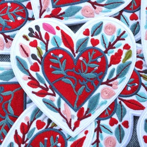 Può includere: Toppe ricamate a forma di cuore con un cuore rosso al centro e disegni floreali. Le toppe presentano ricami rossi, blu, rosa e verdi su sfondo bianco. Ideali per decorare abbigliamento o accessori.