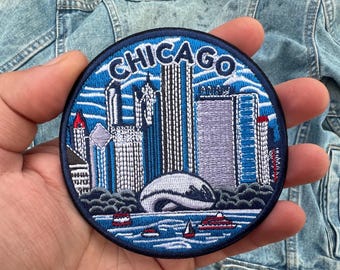 May include: Round embroidered patch featuring the Chicago skyline in shades of blue, white, and red. The patch includes the city name in white lettering, iconic buildings, and a depiction of the Cloud Gate sculpture. Boats sail on the water.