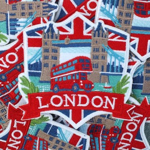 Op de afbeelding: Geborduurde patches met Londense symbolen. Ze tonen een rode dubbeldekkerbus, de Tower Bridge en het woord "LONDON" in wit op een rode banner, tegen de achtergrond van de Union Jack vlag.