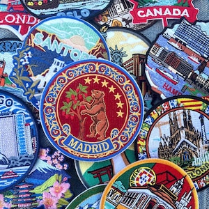 Op de afbeelding: Een verzameling geborduurde patches met verschillende stads- en landontwerpen. De patches bevatten afbeeldingen van bezienswaardigheden, stadsgezichten en vlaggen. De patches zijn in verschillende vormen en maten, met levendige kleuren en gedetailleerde steken.