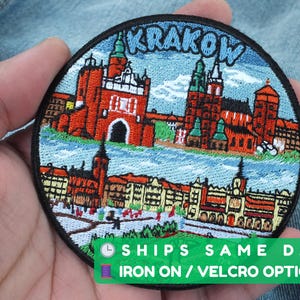 May include: Embroidered patch depicting Krakow, Poland, with detailed buildings and the city name in blue. The round patch has a black border and green accents. The patch is suitable for ironing on or with Velcro.