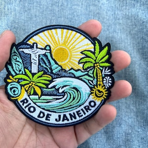 Op de afbeelding: Een ronde geborduurde patch met een Rio de Janeiro-ontwerp. De patch bevat een afbeelding van Christus de Verlosser, palmbomen, een zon en oceaangolven. De woorden "RIO DE JANEIRO" zijn in het wit geborduurd.