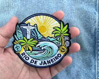 May include: A round embroidered patch featuring a Rio de Janeiro design. The patch includes a depiction of Christ the Redeemer, palm trees, a sun, and ocean waves. The words "RIO DE JANEIRO" are embroidered in white.