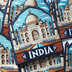 Könnte beinhalten: Gestickte Aufnäher mit dem Taj Mahal in Indien. Die Aufnäher haben einen blauen Himmel mit weißen Wolken. Das Taj Mahal ist weiß mit einer braunen Kuppel. Das Wort "INDIA" ist weiß auf einem marineblauen Banner gestickt.