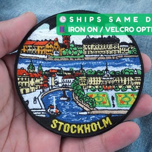 May include: Embroidered patch depicting Stockholm, Sweden, with buildings, water, and the city's name in yellow. The round patch has a black border and is available as an iron-on or Velcro option.