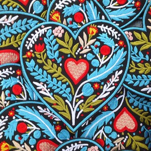 Pode incluir: Patches bordados em forma de coração com fundo preto. Cada patch apresenta um coração vermelho central, rodeado por desenhos florais e de folhas coloridas em azul, verde, branco e vermelho. Ideais para decorar roupas ou acessórios.