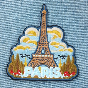 Peut inclure: Écusson brodé représentant la Tour Eiffel à Paris. Le patch a une bordure bleue et le mot "PARIS" en bleu clair. Le design incorpore des couleurs jaune, orange et marron, avec un ciel et des arbres.