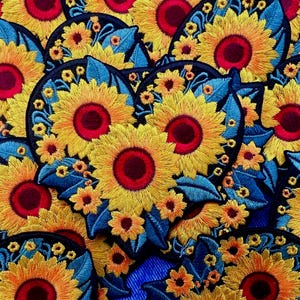 Puede incluir: Parches bordados de girasoles con pétalos amarillos, centros rojos y hojas azules. Los parches son circulares y presentan costuras detalladas, creando un diseño floral vibrante. Ideales para añadir un toque decorativo a ropa o accesorios.
