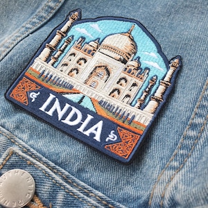 May include: Embroidered patch depicting the Taj Mahal with the word "INDIA" in white. The patch, with a blue border, is sewn onto a denim jacket. The Taj Mahal is rendered in white, beige, and blue hues.