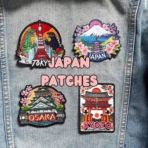 Puede incluir: Cuatro parches bordados con monumentos y ciudades japonesas. Los parches incluyen im&aacute;genes de Godzilla y la Torre de Tokio, el Monte Fuji, el Castillo de Osaka y un templo de Kioto. El texto "TOKY JAPAN PATCHES" est&aacute; escrito en blanco y rosa.