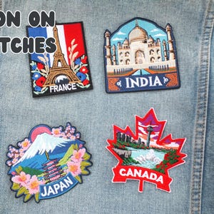Puede incluir: Cuatro parches bordados para planchar que representan monumentos famosos. Los parches incluyen la Torre Eiffel para Francia, el Taj Mahal para India, el Monte Fuji para Jap&oacute;n y una hoja de arce para Canad&aacute;. El texto "IRON ON PATCHES" est&aacute; en la parte superior.