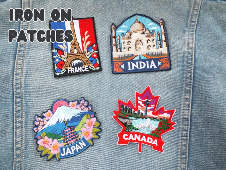 Puede incluir: Cuatro parches bordados para planchar que representan monumentos famosos. Los parches incluyen la Torre Eiffel para Francia, el Taj Mahal para India, el Monte Fuji para Jap&oacute;n y una hoja de arce para Canad&aacute;. El texto "IRON ON PATCHES" est&aacute; en la parte superior.