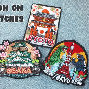 Puede incluir: Parches bordados para planchar con monumentos japoneses e iconos de la cultura pop. Los dise&ntilde;os incluyen un templo de Kioto, el castillo de Osaka y Godzilla con la Torre de Tokio. El texto "IRON ON PATCHES" est&aacute; en la parte superior.